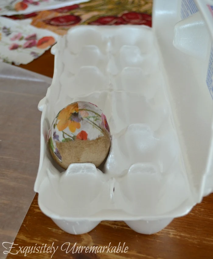 A decoupaged egg in an egg carton