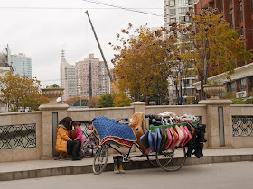 woman sitting with a child next to a tricycle cart filled and covered with items for sale in Shanghai