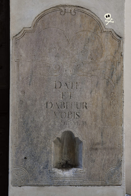 Placa de mármol con grabado de calaveras y cita bíblica. Antiguo limosnero de mármol, con grabado de calaveras y cita bíblica junto a la fecha de restauración del edificio.
