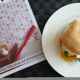 Magazine with a red pen on top of it, next to a plate with a breakfast burger on it.