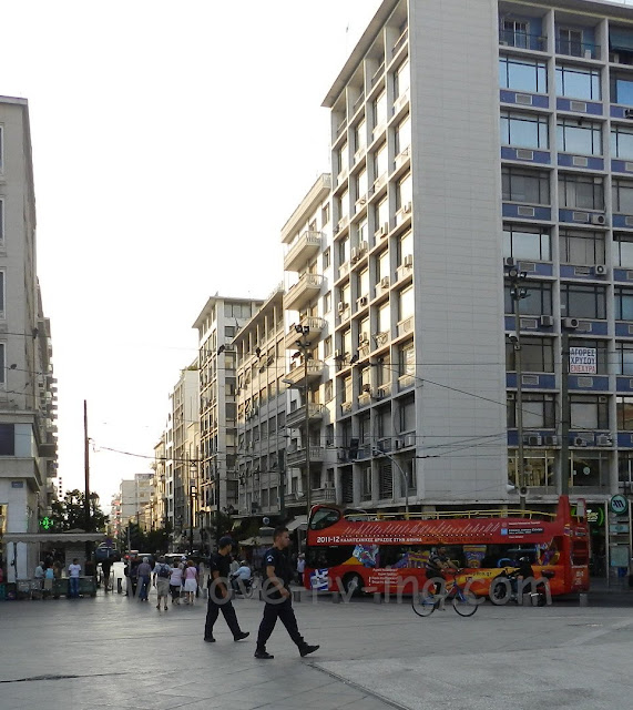 Two policemen walk across Omonia Square while a tourbus stops nearby.