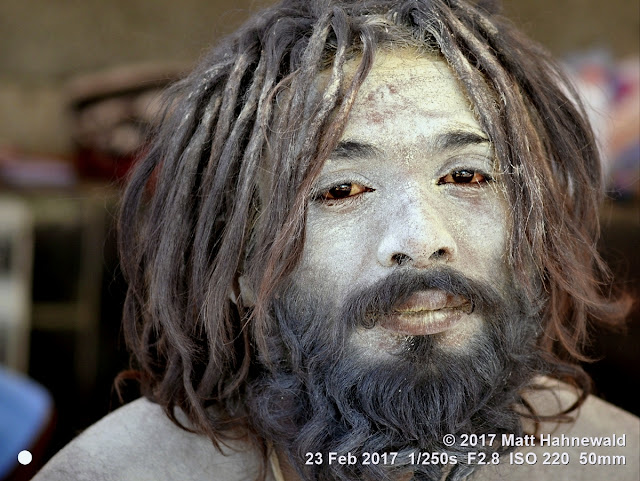 matt hahnewald photography; facing the world; character; face; sacred ash; vibhuti; eyes; bloodshot eyes; facial expression; eye contact; full beard; chin dreads; dreadlock beard; hair; dreadlocks; unkempt; dishevelled; barechested; bareheaded; consent; empathy; rapport; emotion; traveling; spiritual; religious; traditional; cultural; hinduism; shaivism; festival; mela; devotee; worshiper; pilgrim; shivratri mela; bhavnath; junagadh; gujarat; asian; indian; one person; male; adult; young; man; picture; photo; face perception; physiognomy; nikon d3100; nikkor af-s 50mm f/1.8g; prime lens; 50mm lens; 4x3 aspect ratio; horizontal orientation; street; portrait; closeup; headshot; seven-eighths view; white; outdoors; color; sitting; posing; authentic; stoned; yogi; natural frame