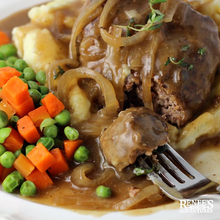 Slow Cooker Salisbury Steak patty cut into with a bite on the fork on a plate with peas and carrots