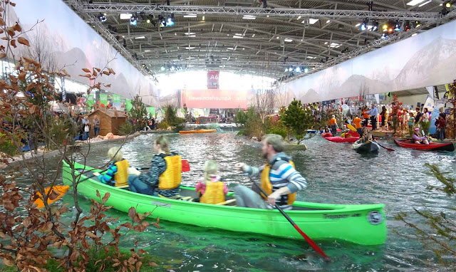 Familie mit Schutzwesten paddelt in grünem Kanu auf der Wasserlandschaft der f.re.e Reisemesse