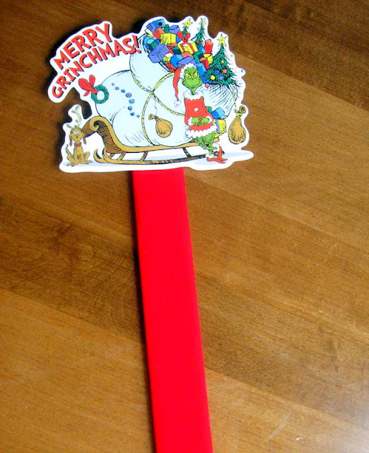 A  grinch gift tag on the end of a red paint stick to  be used as a marker in a homemade Grinch party advent calendar