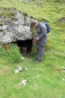 Lotte the German Shepherd standing in the entrance to a small cave, watched by Rich.
