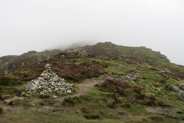 A cairn beside a path through a misty and rocky landscape.