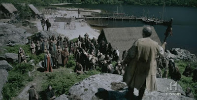 Fotograma de la serie Vikings, en la que se ve una asamblea, donde la gente está reunida y un hombre con un cayado está de pie sobre una roca.