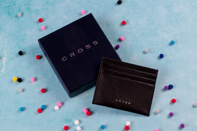 A presentation box with a black leather credit card holder resting on it with CROSS written in small metal writing