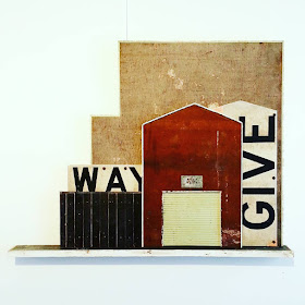 Assemblage art piece by Alex Asch, with various distressed boards making up a 2D view of old warehouse buildings.