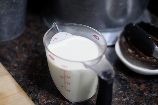 A measuring cup of heavy whipping cream on the counter, coming to room temperature.  