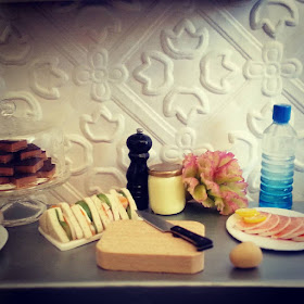 Modern miniature plates of cakes and sandwiches, with the sandwich components laid out on a metal bench top.