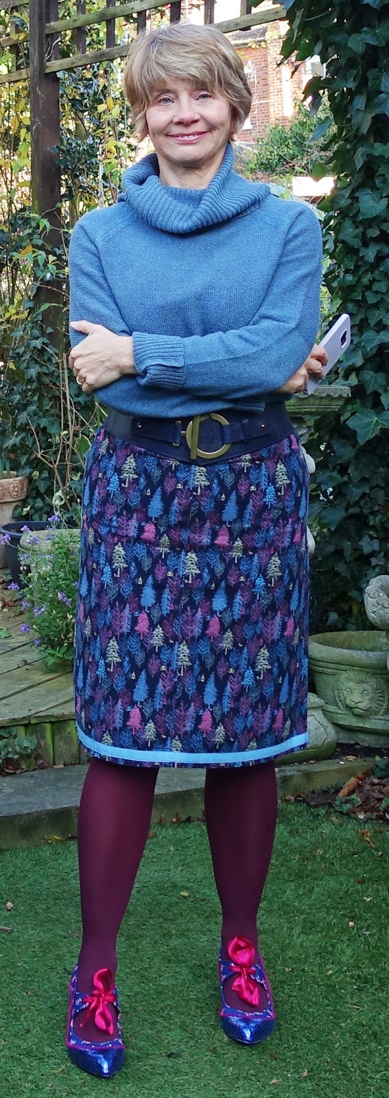 Image showing an over 50s woman in blue cowl neck jumper patterned skirt coloured tights and pink and blue shoes 