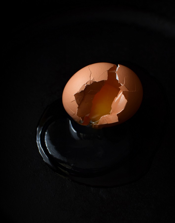 Fotografía de alimentos en clave baja: huevo roto sobre una superficie oscura