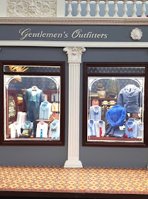 Detail of the front of a one-twelfth scale men's clothing shop with two display windows full of various men's clothing.