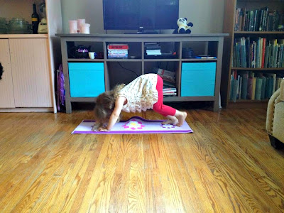 Photo of young girl on a yoga mat doing the 'downward dog' pose in the living room--with wooden floors