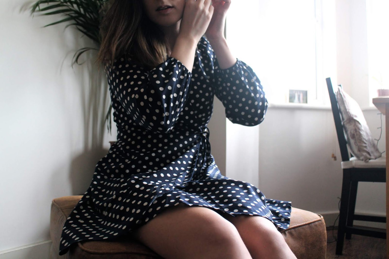 Girl in navy blue polka dot dress sat on a footstool