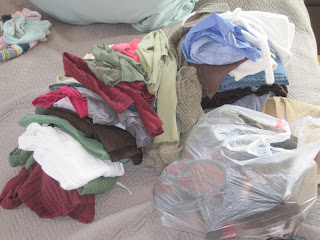 Pile of sweaters, tops, pants, and trash bag full of shoes