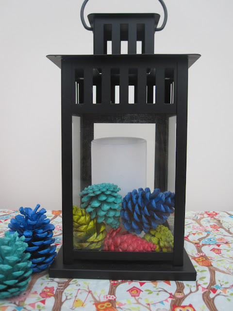 Painted pine cones in a black lantern with an led candle