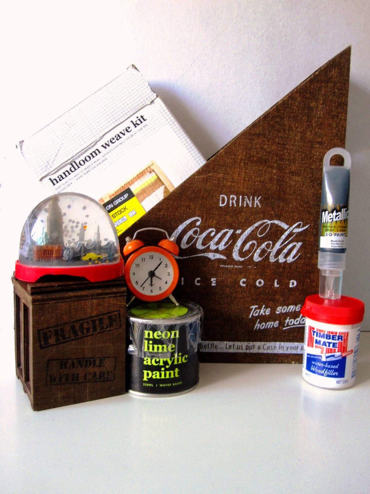 A selection of items from Typo (including a wooden Coca Cola magazine holder,a handlloom weave kit, a snow dome, tin of neon lime paint and a small orange alarm clock, Plus a small container of wood filler and a tube of  3D paint.