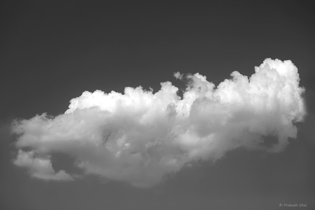 A Black and White Look Up Minimalist Photograph of a Wandering Cloud travelling across the Sky.