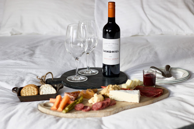 Charcuterie board on bed with Sandhill Wine Bottle