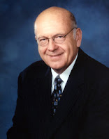 Bald, bespectacled middle aged white man wearing a suit and tie.