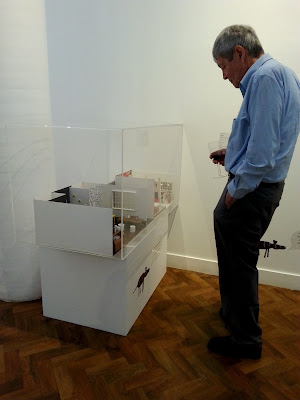 Man looking at a miniature scene exhibited in a gallery.