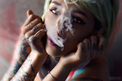 Chica rubia con tatuajes fumando con humo hacia la cámara