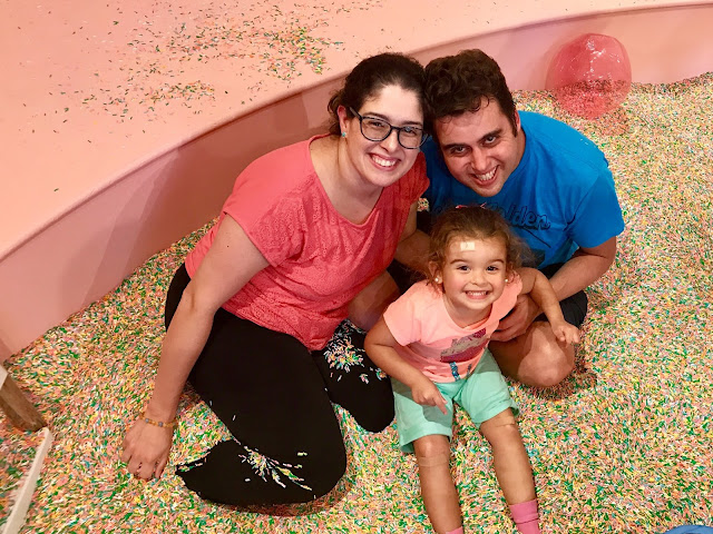 A family of three pose smiling for a photo in a pool full of colorful sprinkles