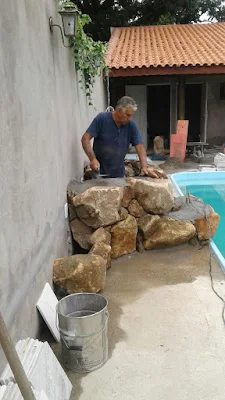 Bizzarri trabalhando, fazendo uma cascata de pedra na piscina com pedras ornamentais tipo pedra moledo na cor bege.