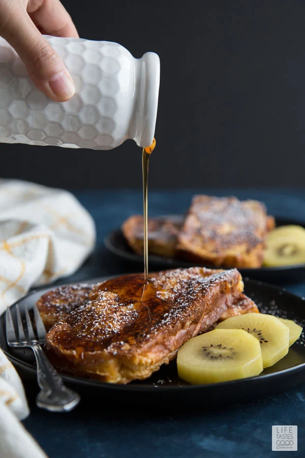 A plate of Alton Brown French Toast with kiwi slices and maple syrup being drizzled over the toast