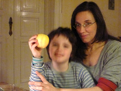 Frau und Kind (verschwommen) im Abendlicht einer Wohnung, der Kleine präsentiert einen Apfel.