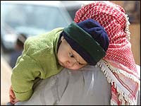 An Iraqi refugee carries his son at a refugee camp near the far eastern Jordanian town of Ruweished, March 29, 2003. [NPR - Corbis]