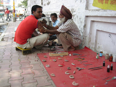A man giving tattoos on the street corner next to a man making dentures.