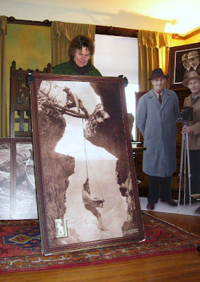 Ranger James shows historic photo of Ellsworth holding a rope with Emery hanging