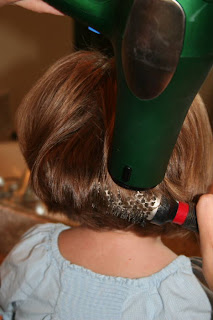 Back view of young girl's hair being styled with a blow dryer and round brush