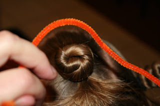 Close up view of young girl's hair being styled into "Holiday Twisty Buns" hairstyle with an orange pipe cleaner