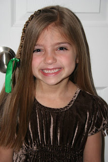 Portrait view of young girl modeling "Teen Slide-Up Braid" hairstyle outside styled with green ribbon hair accessory