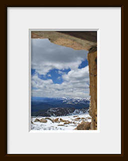 A framed photo of looking out a rustic window from the ruins of a chalet at the very top of Mount Evans at an elevation of 14,264' shows a scenic mountain landscape as far as the eye can see.