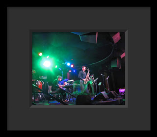 A sax player moves trailing green streamers on the stage of a small night club.