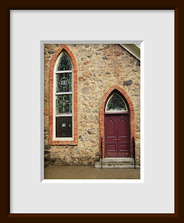 The burgundy doors and stained glass window of a stone Gothic church are outlined with beautiful brick arches.