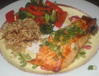 plate of grilled salmon covered in green onions with a side of brown rice and red peppers and broccoli
