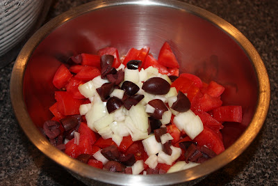 large silver bowl with diced tomatoes, white onions, and kalamata olives