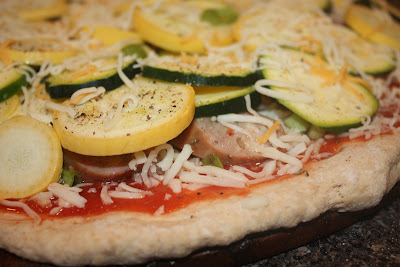 close up of uncooked pizza dough topped with tomato sauce, cheese, sausage, zucchini, and squash