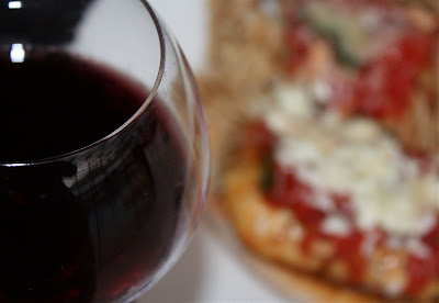 glass of red wine with chicken parmesan dish out of focus in the background