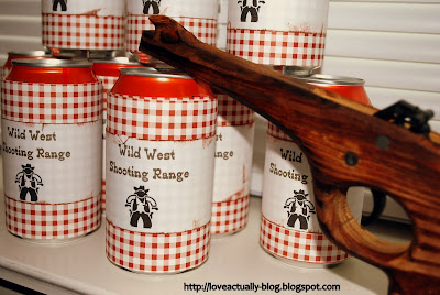 Soda cans that read "Wild West Shooting Range" and a wooden rubber band gun. 