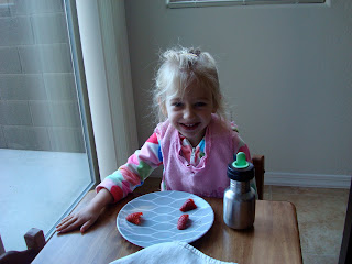 Young girl sitting at Childs table eating a plate of strawberries