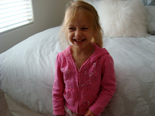 Young girl standing in front of bed smiling