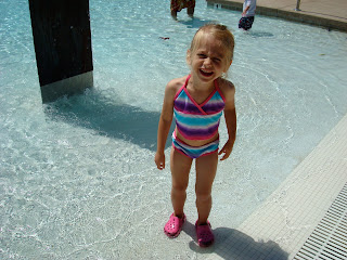 Young girl in swimsuit and crocs wading in pool  